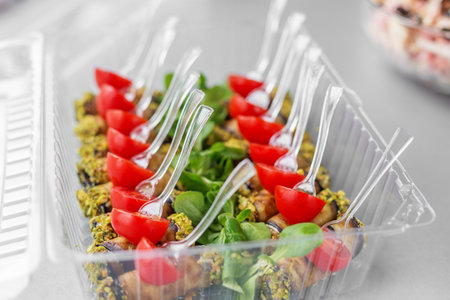 Close-up of pistachio-coated eggplant rolls with cherry tomato halves, served in plastic forks over greens, ready for catering delivery.の写真素材