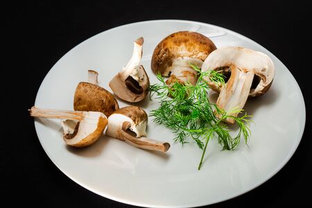 In the center is a white plate on a black background with royal mushrooms and green dillの写真素材