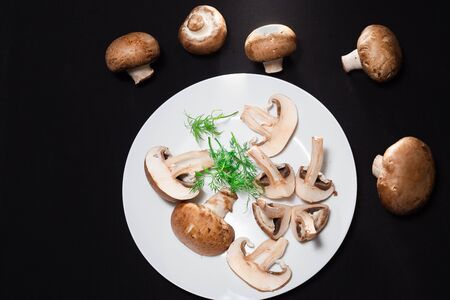 In the center is a white plate on a black background with royal mushrooms and green dillの写真素材