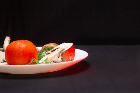 In the center is a white plate on a black background with royal mushrooms and green dill, red tomatoの写真素材