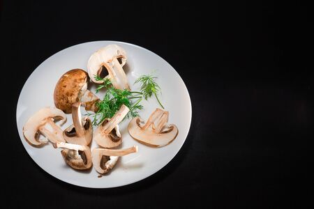 In the center is a white plate on a black background with royal mushrooms and green dillの写真素材