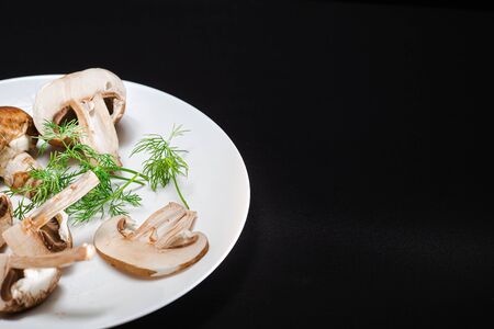 In the center is a white plate on a black background with royal mushrooms and green dillの写真素材
