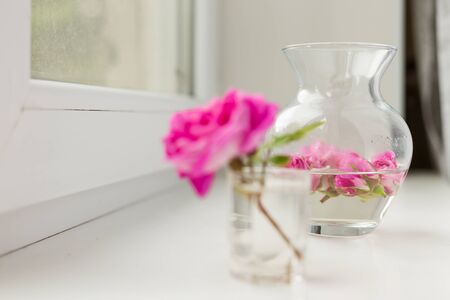 On a windowsill there is a vase with water and bars of pink rosesの写真素材