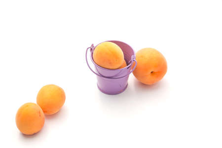 Orange apricots on a white background with a lilac bucketの写真素材