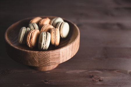 Several multi-colored macaroons in a wooden plate on a rustic wooden brown table. Place for text.の写真素材