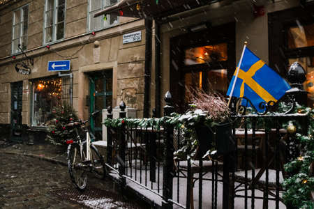 Swedish flag waving in the snow, outside a cafe in the tourist hotspot Gamla Stan, Stockholm, Sweden.の写真素材