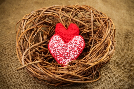 Two red handmade hearts in the nest on the sacking backgroundの写真素材