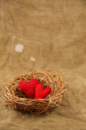 Two red handmade hearts in the nest on sackcloth backgroundの写真素材