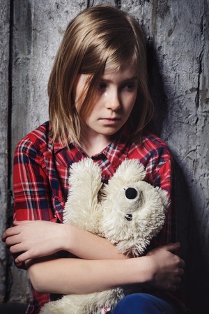 Depressed alone crying girl sitting with toy near wallの写真素材