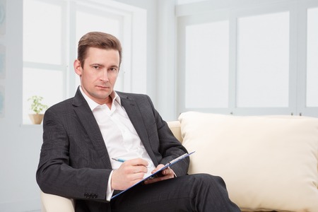 male psychologist  being ready to take notes  sitting on the couchの写真素材