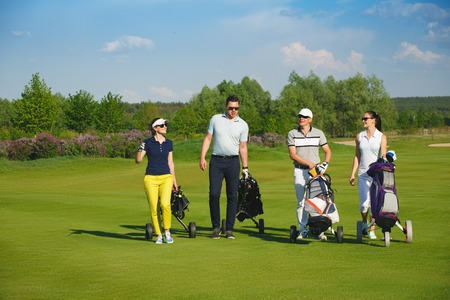 Four friends golfers walking on golf course at sunny dayの写真素材
