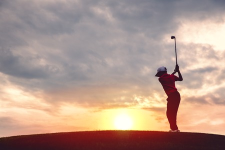 silhouette of boy golfer with golf club at sunsetの写真素材