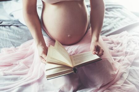 pregnancy and leisure concept - pregnant woman reading book in bed at homeの写真素材