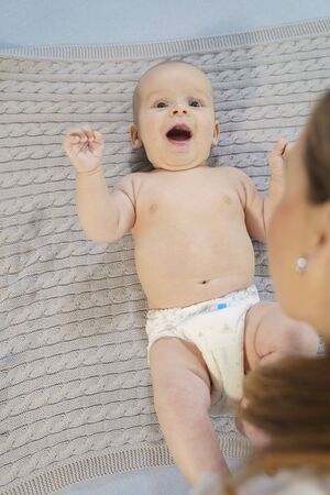 Funny little baby playing with mom on a knitted blanket