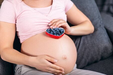 Young pregnant woman holding a bowl of blueberries in her hands showing a healthy approach to the pregnancyの写真素材