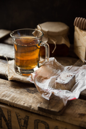 Glass cup with hot tea with honey or jam jar of, wood spoon, Spanish polvoron on vintage cookie box, black wall background, inside rustic countryside, cozy atmosphereの写真素材