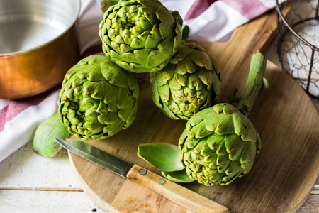 Fresh ripe green artichokes on cutting board, knife, copper dipper in the background, kitchen table, top viewの写真素材