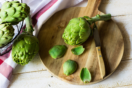 Peeled fresh artichoke preparing for cooking, wood cutting board, knife, vegetables in metal basket, rusticの写真素材