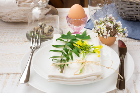 Easter table setting, white plates, cutlery, napkin, flowers in eggshell, green twigs, crystal cup,...