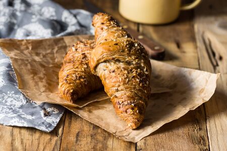Whole wheat croissants with sesame seeds on wood kitchen table towel enamel mug. Breakfast cozy morning atmosphereの写真素材