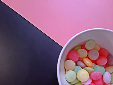 Black and Pink color paper in diagonal intersection with soft focus colorful candy in lower right...