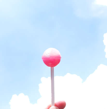 A lollipop to the bright blue sky and white clouds showing good wishes and positive emotions.の写真素材