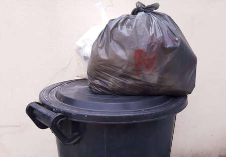 Plastic bag of garbage put on top of rubbish bin.
