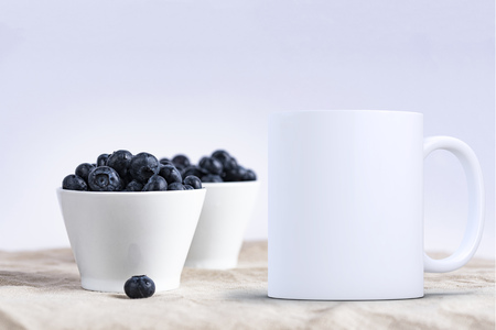 White blank coffee mug mock up, in front of two bowls of blueberries, add custom design or quote on to the mug.の写真素材