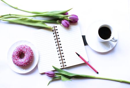 A business man's Breakfast is coffee, a Notepad, a pink donut, and delicate lilac tulips. Background for greetings, invitations, and postcards.の写真素材