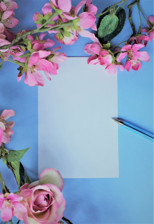 Blank paper with pink flowers on blue background. Flat lay, top view.の写真素材