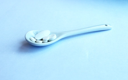 White pills in a spoon on a blue background. Focus on foreground.