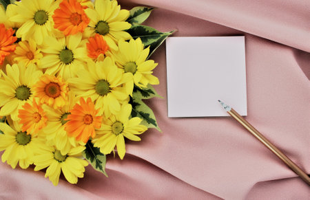Bouquet of yellow daisies and a sheet of paper on a pink fabricの写真素材