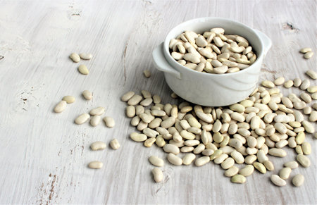 White beans in a bowl on a white wooden background, selective focus