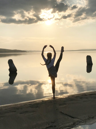 Silhouette of young woman practicing yoga on the beach at sunsetの写真素材