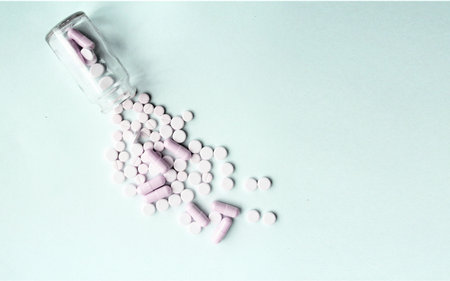 White and pink pills spilling out of a bottle on a white background