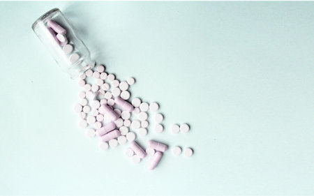 Pink and white pills spilling out of a bottle on a blue backgroundの写真素材