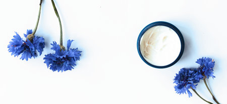 cosmetic cream and blue cornflowers on a white background.の写真素材