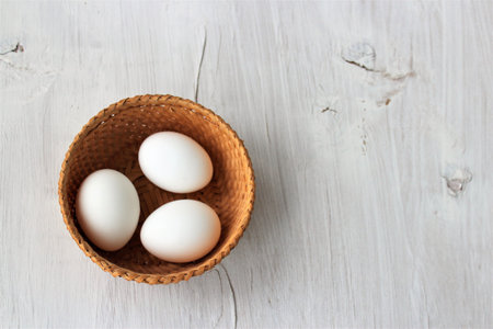 White eggs in a wicker basket on a white wooden background.の写真素材