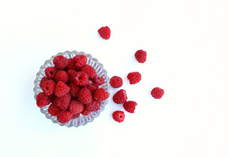 Raspberries in a glass bowl on a white background, top view