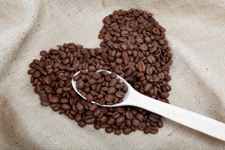 Heart of the coffee beans and wooden spoon on sackingの写真素材