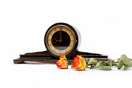 antique wooden table clock and dry roses on a white background.