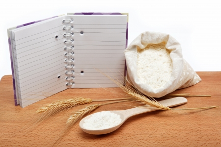 Recipe Book and flour in a sack with a spoon on a wooden table.の写真素材