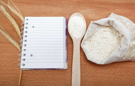 Recipe Book and flour in a sack with a spoon on a wooden table.の写真素材
