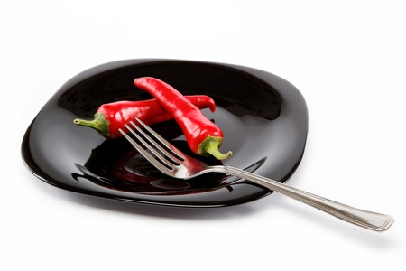 Red hot chili peppers in a black plate with a fork, isolated on white background.の写真素材