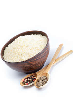 Grains of rice in a bowl and two wooden spoons with spices isolated on white background.の写真素材