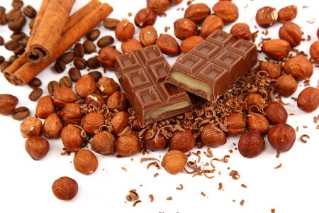 Stack of chocolate tiles with hazelnuts and cinnamon sticks on a white background.の写真素材