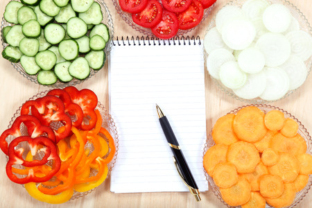 Notebook for recipes and vegetables on wooden table.の写真素材