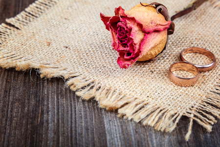 Wedding rings and roses dried flowers on wooden background.の写真素材