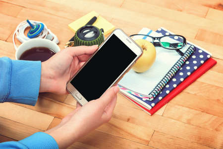 Female hand with a mobile phone, notebooks, pen, glasses, music speakers, headphones, cup of tea,...
