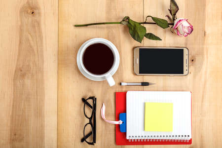 Mobile phone, glasses, a cup of tea, flowers, stationery, headphones, musical speaker on a wooden...